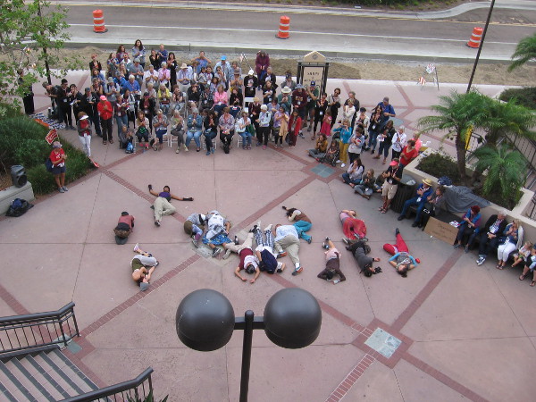 The dancers collapse and lie on the concrete.
