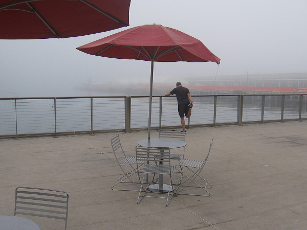 A jogger stretches on the observation platform near Broadway Pier, beside the fog covered water.