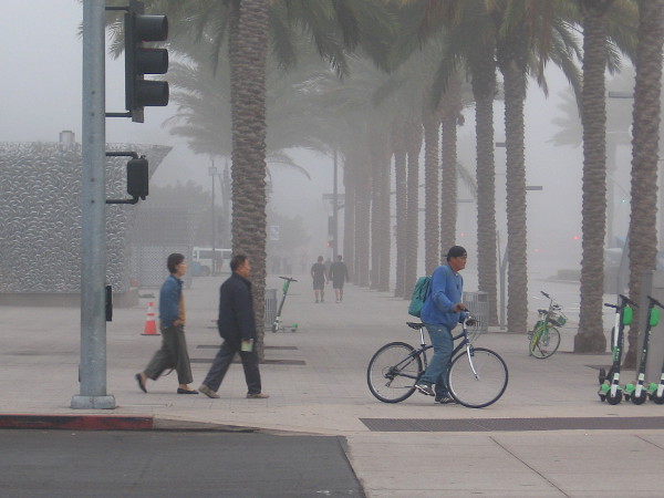 People head down the sidewalk in the early morning fog.