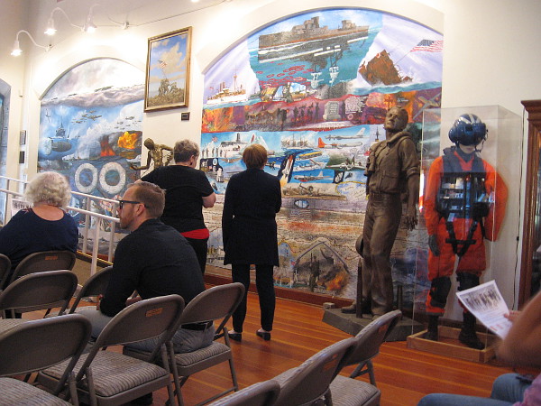 Visitors to the Veterans Museum look at a large mural on one wall before the program begins.