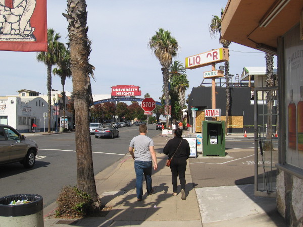 People walk up the Park Boulevard sidewalk toward the University Heights landmark sign.