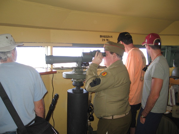 A docent in a World War II era uniform demonstrates the use of an azimuth scope, used to scan the ocean for enemy vessels during the war. These spotting scopes gave accurate readings of target positions.