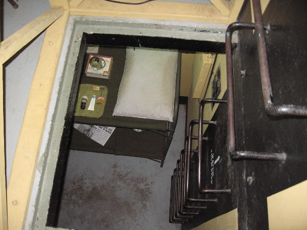 Metal rungs descend into the lower level of the bunker, where visitors can see the small bunkroom and a typical Base End Station.