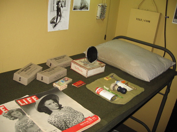 Objects in the bunkroom include toiletries, U. S. Army rations, cigarettes, magazines and pin-ups on the wall.