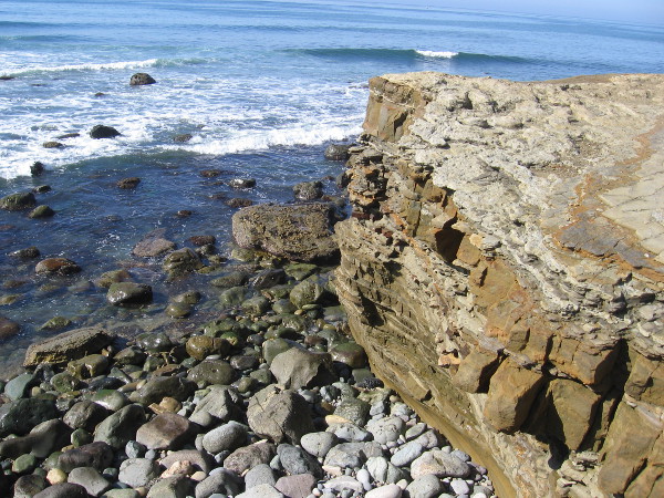 As we head down a short dirt path from the overlook to the tidepool area, we take a closer look at the eroded sandstone cliffs and water-smoothed stones on the narrow beach below.