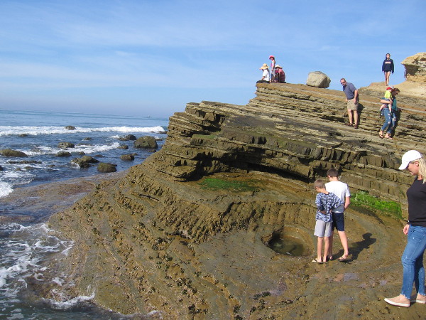 People explore a smooth bowl-like pit in the eroded, layered, uptilted sandstone.