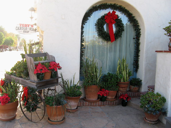 Poinsettias on an old-fashioned cart, and a window wreath decorate one corner of Toby's Candle and Soap Shop.
