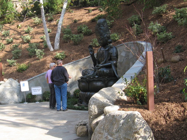 Visitors to the Japanese Friendship Garden gaze at Kannon Bosatsu, a nearly three century old 5750 pound bronze statue recently installed in the Lower Garden by crane!