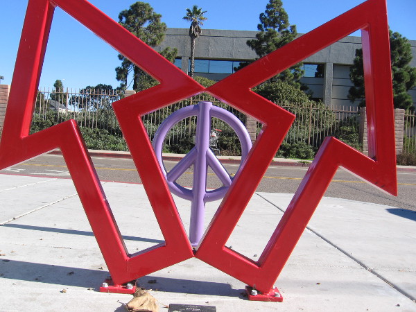 Photo of two cool sculptures in National City. A lavender peace sign is framed by two red arrows!