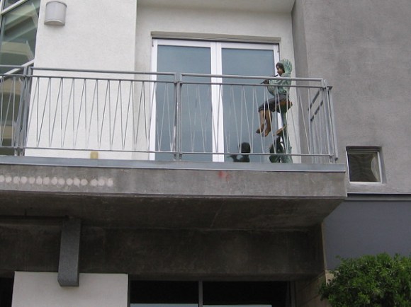 A boy plays a flute up on someone's balcony.