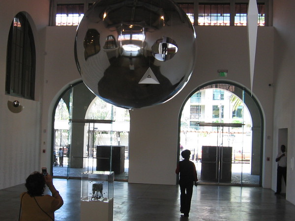 A large silvery orb is suspended from the ceiling of the Iris and Matthew Strauss Gallery, inside MCASD's historic Joan and Irwin Jacobs Building.
