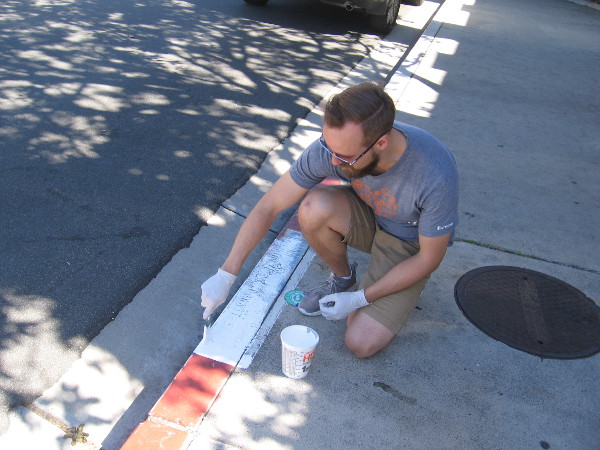 Volunteer on a sidewalk in Liberty Station applies a new coat of paint on the curb above a storm drain.