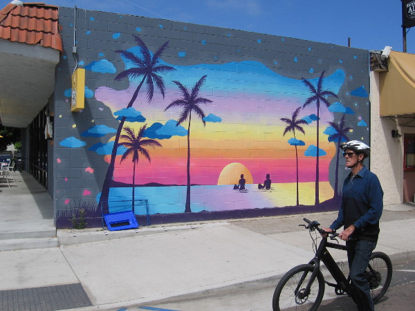 Someone rides their bike down Highway 101 past this beach sunset mural by @CloeHakakian