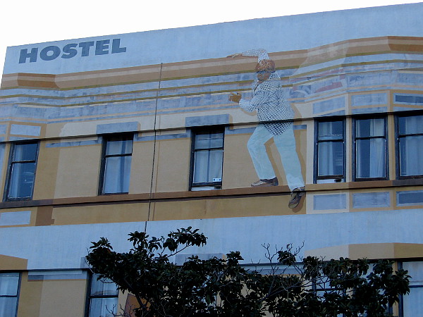 A guy hanging from the roof of a hostel.