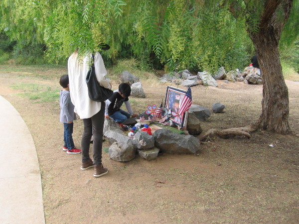 A family in Escondido's Kit Carson Park pauses to gaze at a small memorial.
