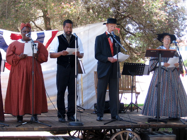 Diverse people in period costume read segments of the Declaration of Independence.