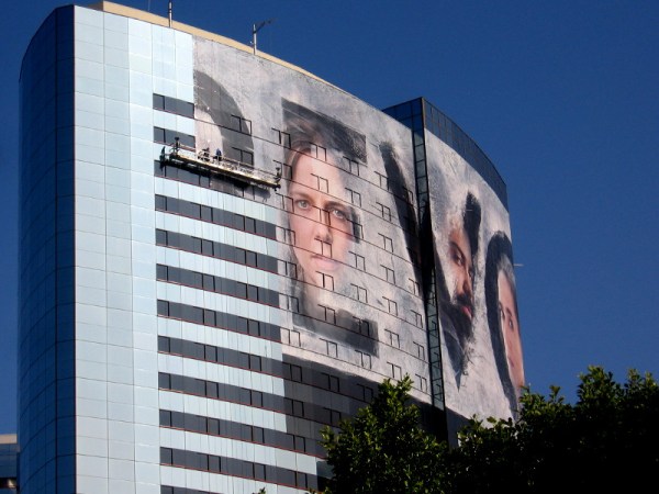 Workers apply large format printed wrap material to the side of one tower.