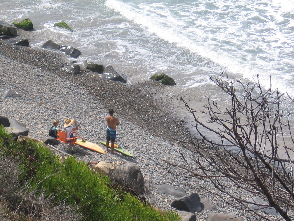 People gaze at the foaming water from a rocky beach.