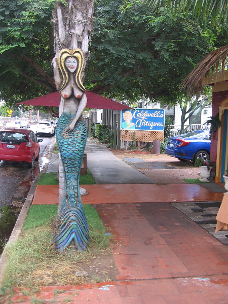 A very tall carved mermaid by the sidewalk.