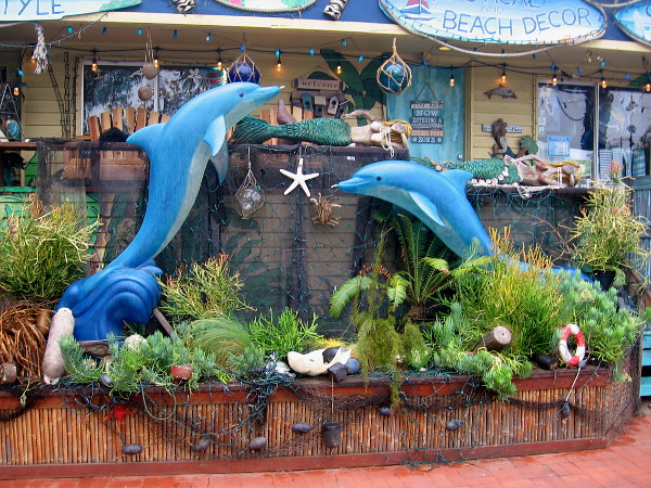 Two dolphins leap by the sidewalk.