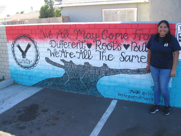 Muralist Nadia Sanchez smiles near her new artwork. We All May Come From Different Roots But We Are All The Same.