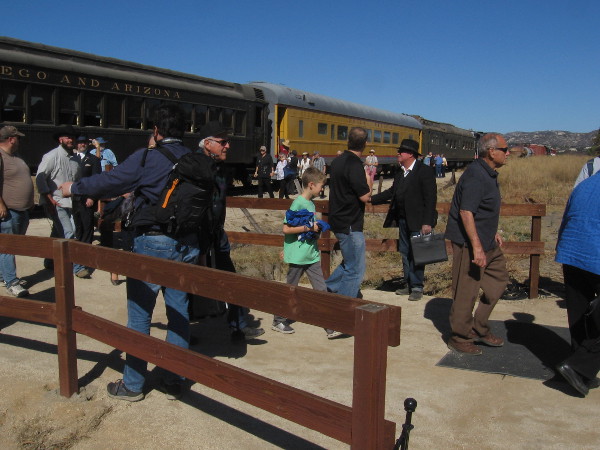 Passengers disembark from the day's first excursion train and arrive at the outdoor venue for the gold spike event, near the museum's Display Building.