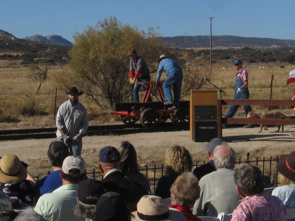 The gold spike reenactment begins. Railroad workers arrive by handcar.