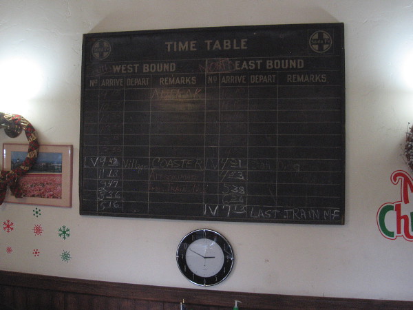 A board on the wall shows arrival times for Amtrak and the Coaster. The active Carlsbad Village train station is one block north.