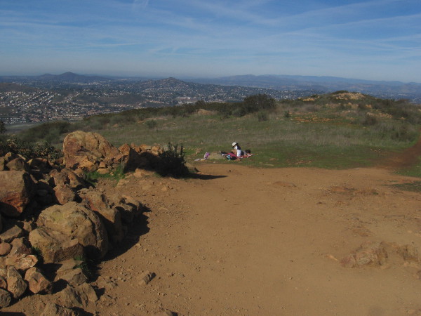 A couple of hikers brought a blanket to rest on the grass beneath the sky.