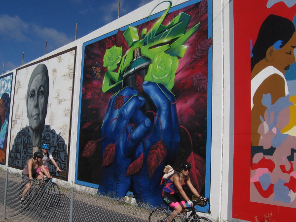 People bicycle past huge colorful murals painted along the Bayshore Bikeway in Chula Vista.