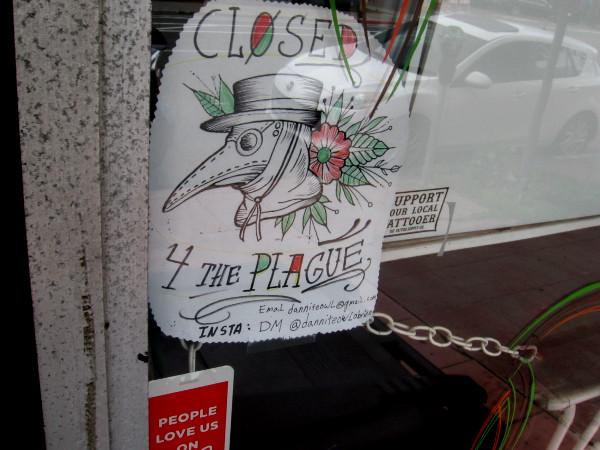 A tattoo parlor has a graphic in their window. Closed 4 the plague.