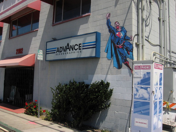 A superhero who resembles Superman flies from what might be San Diego's last phone booth.
