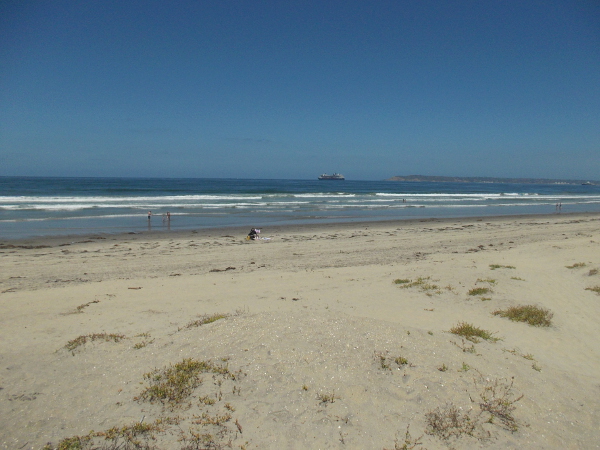 The blue Pacific Ocean stretches beyond the seemingly barren western shore of the Silver Strand. Point Loma and a cruise ship can be seen in the distance.