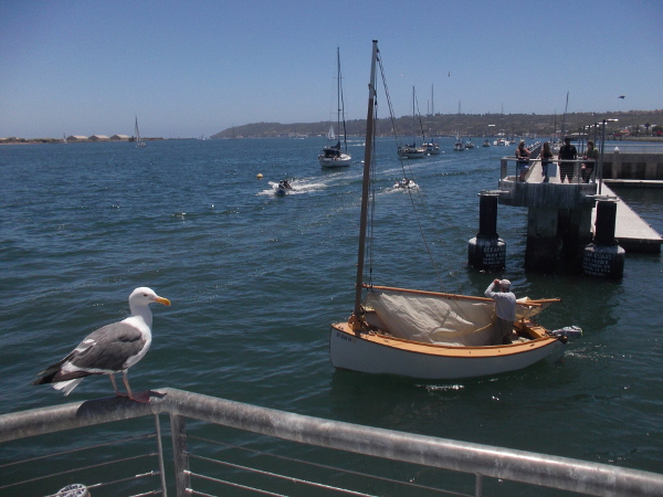 A cool little wooden sailboat sets out into the bay.
