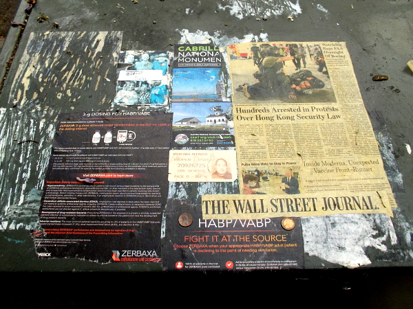 A mysterious paper collage on top of a sidewalk electrical box.