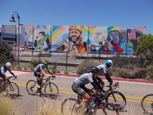 Cyclists following the Bayshore Bikeway head north on Marina Way past a mural on a building at the National City Marine Terminal.