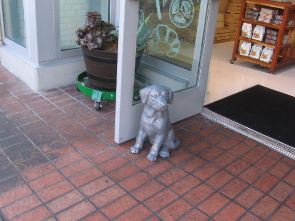 Sculpted dog holds open a shop door.